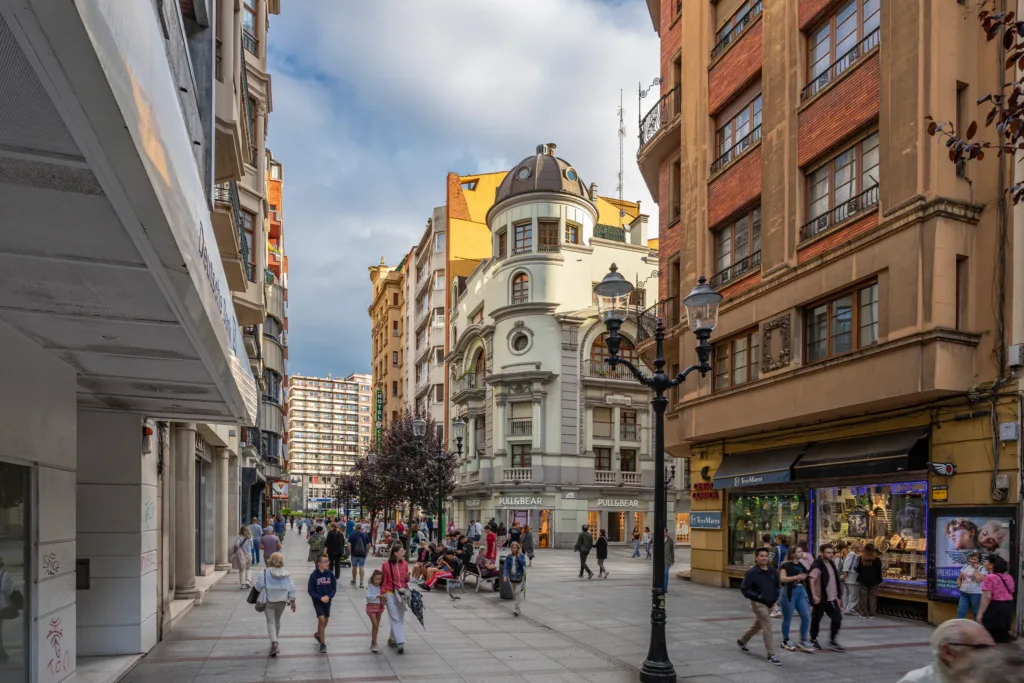 Calle peatonal con edificios, comercios, farolas y personas caminando.